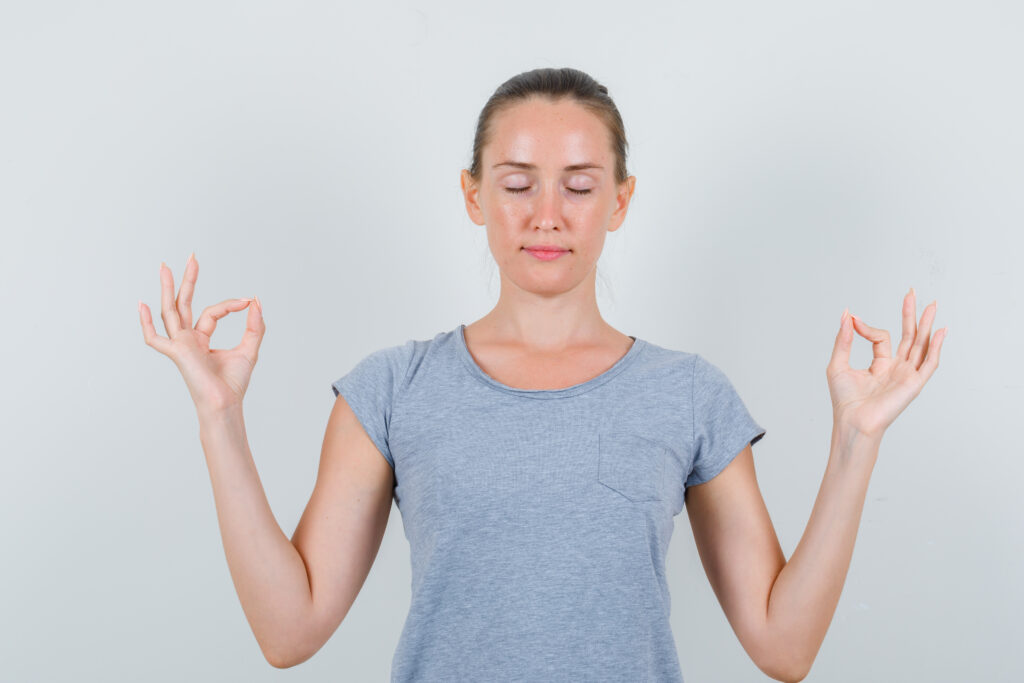 Young female doing meditation with closed eyes in grey t shirt and looking peaceful , front view.